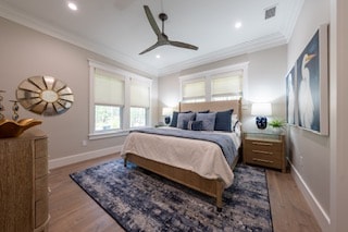 Neutral coastal bedroom with wood furnishings, navy rug, and roller shades