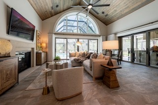 Vaulted living room with arched window, neutral seating, and wood ceiling